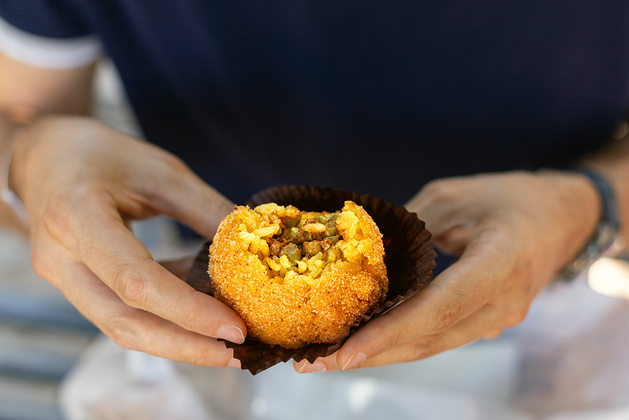A man eating arancini, italian rice ball al ragu or al sugo, that is stuffed with meat, peas and tomato sauce and spices, coated with breadcrumbs and deep fried. Sicilian street food, cuisine.